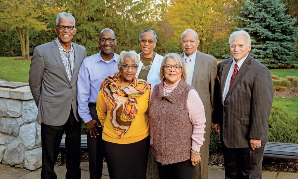 Seven people gathered by a stone wall with fall trees in the background